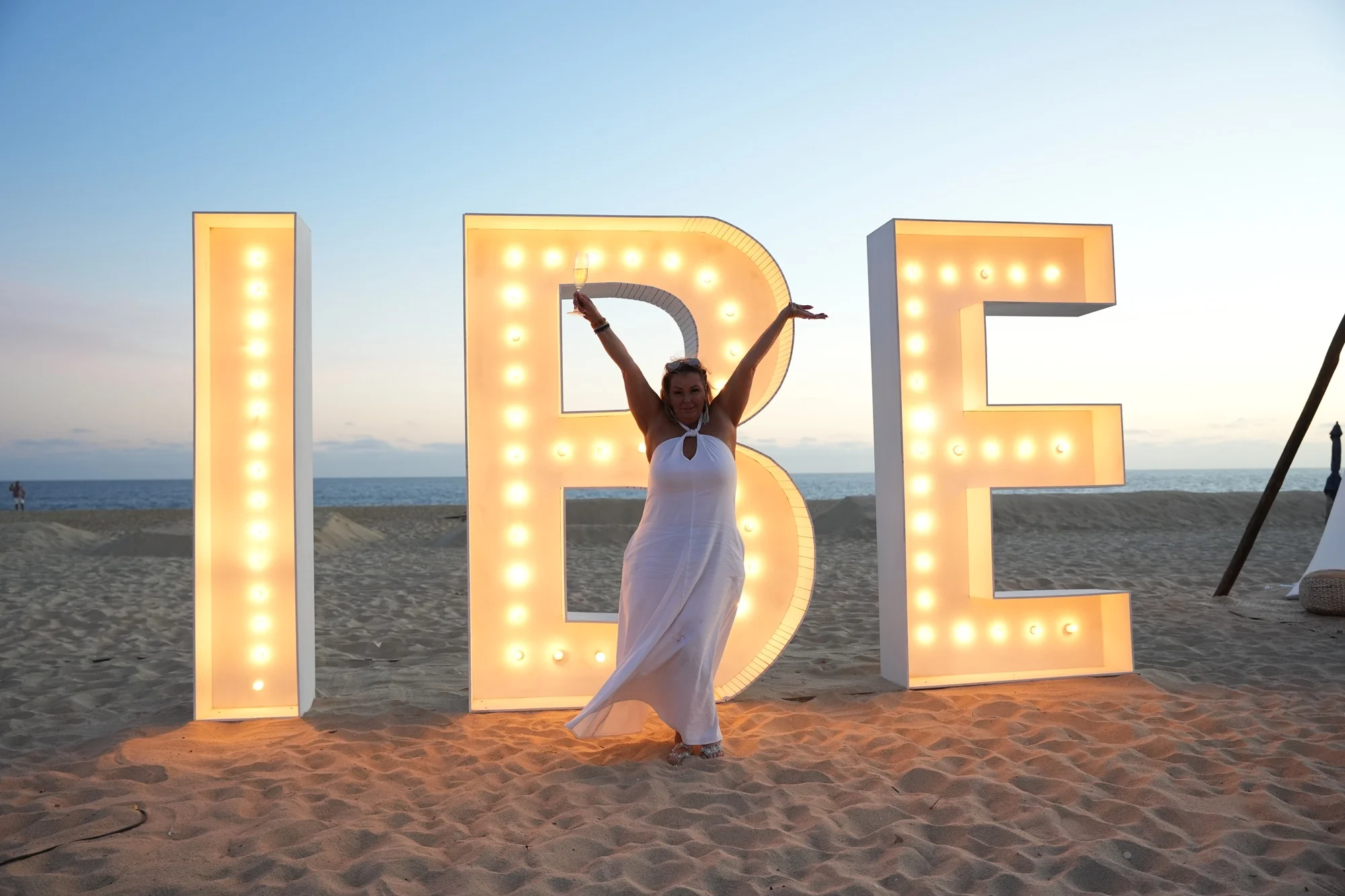 Mel at the IBE event in front of illuminated IBE letters on the beach